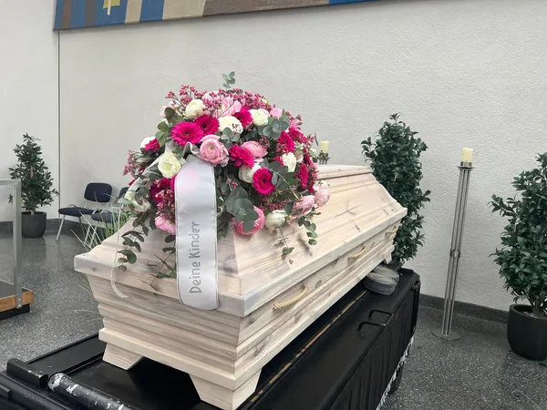 Heller Sarg in der Trauerhalle mit einem Gesteck aus pinken und weißen Blüten