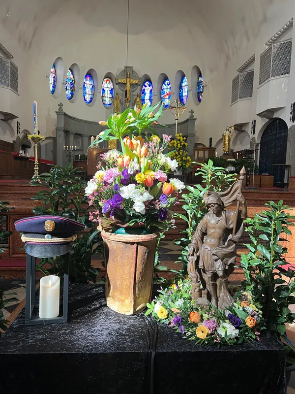Urne mit Frühlingsgesteck vor dem Altar, daneben eine Florian-Figur, eine Dienstmütze und eine Kerze in einer Laterne