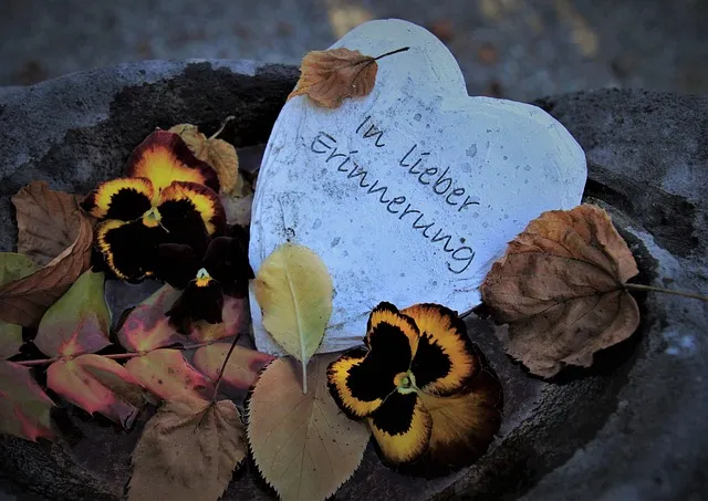 Herz aus Stein mit der Aufschrift „In lieber Erinnerung“, umgeben von Herbstlaub